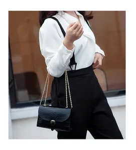 Close-up detail of a black crocodile pattern chain bag worn with a white blouse and black pants