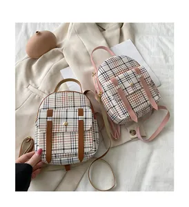 Macro detail of two small plaid backpacks with leather accents on a cream background