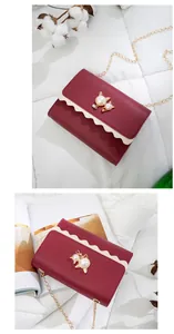 Detail showing a red crossbody bag with cute cat-shaped pearl ornaments and a gold chain.