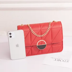 Borsa a tracolla trapuntata rossa con catena d'oro accanto a uno smartphone bianco