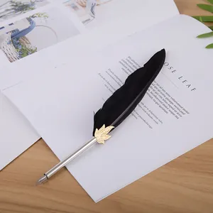 Plume d'oie noire élégante avec accent feuille d'or posée sur un magazine vintage.