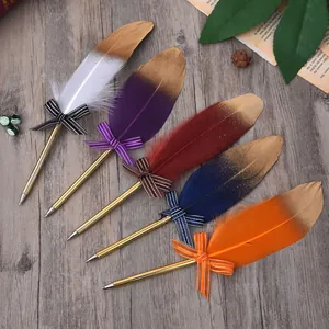 Close-up of five colorful feather pens with gold glitter and bows on wood background
