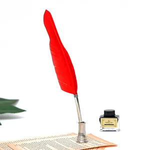 Détail d'une plume d'oie rouge vintage dans un support argenté avec bouteille d'encre