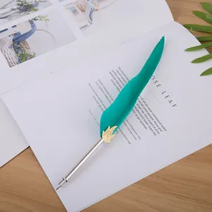 Détail d'un élégant stylo plume en plumes turquoise avec feuille d'or sur un livre.