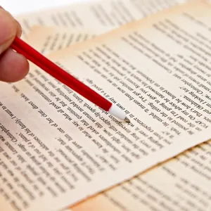 Close-up of a red feather ballpoint pen pointing at text on vintage book pages