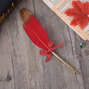 Red and gold feather ballpoint pen with a bow decoration on wood background