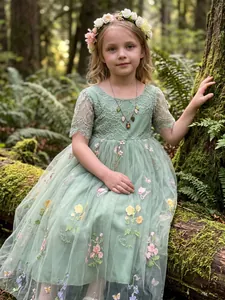 Detail view of a green lace fairy dress with floral embroidery in a forest setting.