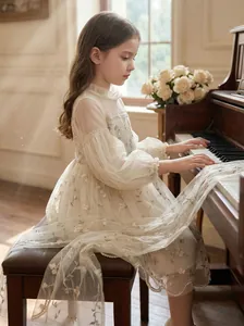 Detail view of elegant girl's mesh dress with floral vine embroidery in a piano room setting