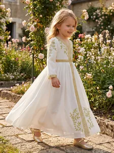 Elegant white girls' ethnic dress with gold embroidery in a sunlit garden setting.