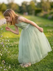 Elegant young girl wearing a sage green tulle flower girl dress in a sunny garden setting