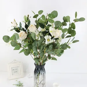 Ramas de eucalipto artificial y rosas blancas en un elegante jarrón de vidrio decorativo