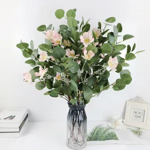 Detalle de hojas de eucalipto artificiales y flores rosas en un jarrón de cristal