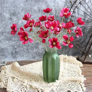 Dettaglio di fiori di cosmo in seta rosa scuro in un vaso verde opaco per decorazioni.