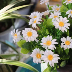 Close-up detail view of artificial white daisies featuring vibrant yellow centers and green leaves.