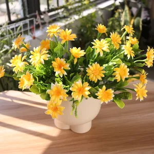 Vibrant yellow artificial chamomile daisies in a creative white pot on a sunlit balcony table
