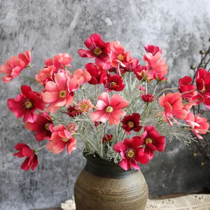 Vista dettagliata di fiori di cosmo artificiali in seta rosa e rossa in un vaso rustico.