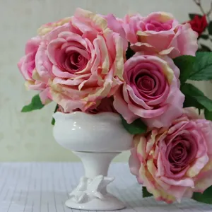 Close-up of seven pink artificial curled edge roses in a white ceramic vase
