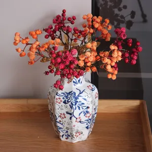 Vibrant red and orange artificial berry branches in a classic ceramic vase