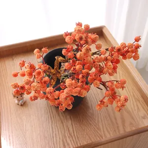 Detailed view of textured artificial orange pomegranate berry stems in a dark ceramic pot