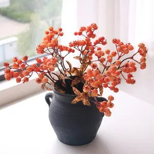 Close-up of decorative artificial pomegranate branches in a rustic dark ceramic vase.