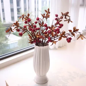 Artificial red pomegranate branches in a white fluted ceramic vase for home decor