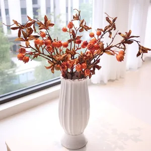 Detail of artificial pomegranate branches in a white fluted ceramic vase for home decor