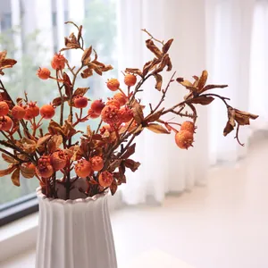 Detailed macro view of artificial pomegranate fruit branch in white ceramic vase