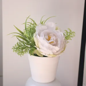 Close-up of white artificial peony potted plant with green leaves in a minimalist white vase.