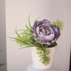 Close-up of realistic purple artificial peony flower with lush green foliage in white pot