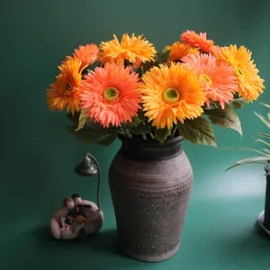 Close-up of vibrant artificial orange gerbera daisies arranged in a textured grey vase.