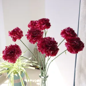 Vue détaillée d'œillets artificiels en soie rouge foncé disposés dans un vase en verre clair.