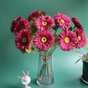 Detailed view of artificial magenta gerbera daisies in a gold-rimmed glass vase.