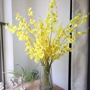 Macro view of artificial yellow dancing lady orchids in a glass vase on a wooden table.