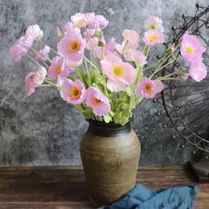 Primer plano de amapolas artificiales rosas en un jarrón de cerámica vintage.