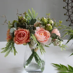 Close-up of pink Penglai peony artificial flowers in a clear glass vase with green foliage