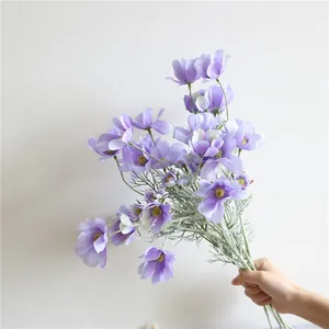 Vista dettagliata di fiori di cosmo viola artificiali di alta qualità tenuti in mano