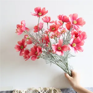 Dettaglio di un bouquet di fiori di cosmo artificiali in seta rosa tenuto in mano.