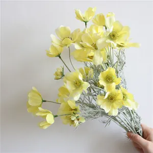 Dettaglio macro di fiori finti cosmos in seta gialla tenuti in mano per decorazioni nuziali.