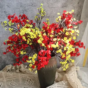 Flores de paniculata de seda rojas y amarillas en un jarrón sobre mantel de encaje