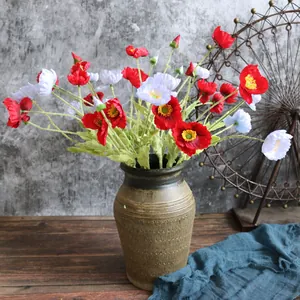 Detalle de amapolas de Islandia artificiales rojas y blancas en un jarrón rústico de cerámica