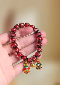 Gros plan d'un bracelet en perles de verre rouges avec des breloques dorées.