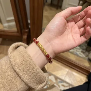 Gros plan d'un bracelet en agate rouge et perles d'or texturées porté au poignet.