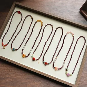 Eleganti collane di granato naturale con gemme multicolori presentate in un vassoio di legno