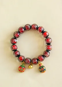 Gros plan détaillé du bracelet en verre émaillé rouge avec des breloques dorées d'aspect