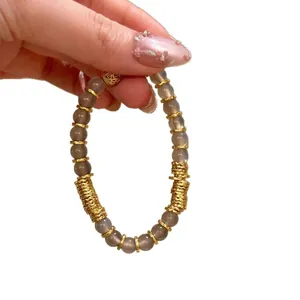 Bracelet élégant en agate grise naturelle avec breloques dorées sur fond blanc neutre