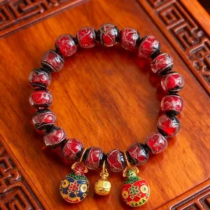 Bracelet artisanal en perles de verre rouge avec breloques sur un plateau en bois sculpté
