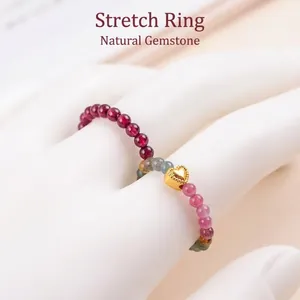 Detailansicht eines elastischen Perlenrings mit Turmalin und goldenem Herzanhänger am Finger