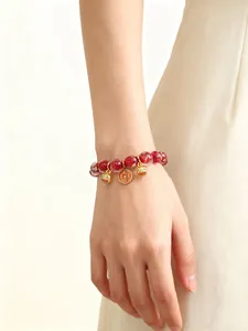 Detailansicht eines roten Glasperlenarmbands mit goldenen Glücksbringern am Handgelenk