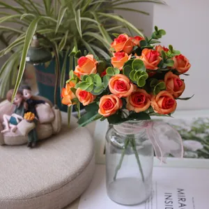 Close-up detail of artificial orange rose bouquet with green eucalyptus in clear glass vase