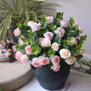 Detailed view of artificial pink roses and eucalyptus leaves arranged in a dark blue vase